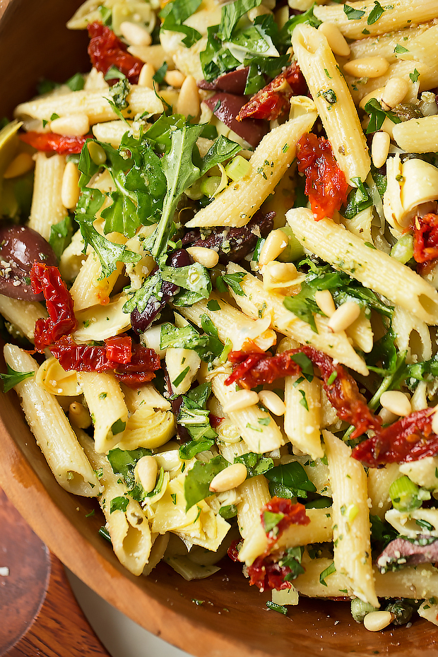 Italian pasta salad in bowl with pine nuts, arugula, sun-dried tomatoes and penne