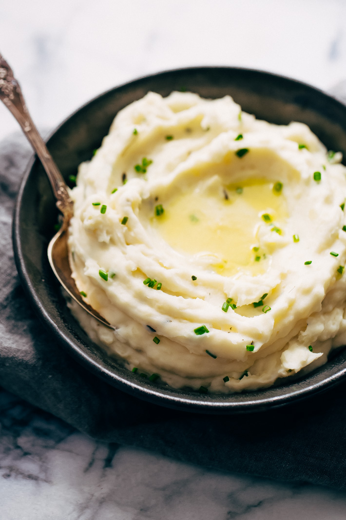 mashed potatoes topped with chives and melted butter in bowls with spoon