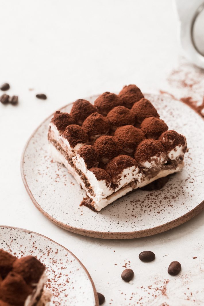 square of eggless tiramisu on a speckled plate dusted with cocoa powder