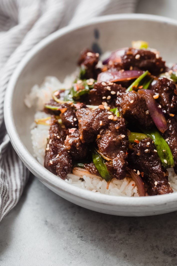 close up shot of crispy beef with sesame seeds and scallions on jasmine rice