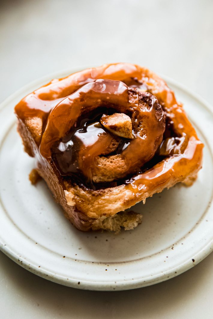 cinnamon roll on speckled plate with caramel sauce on top