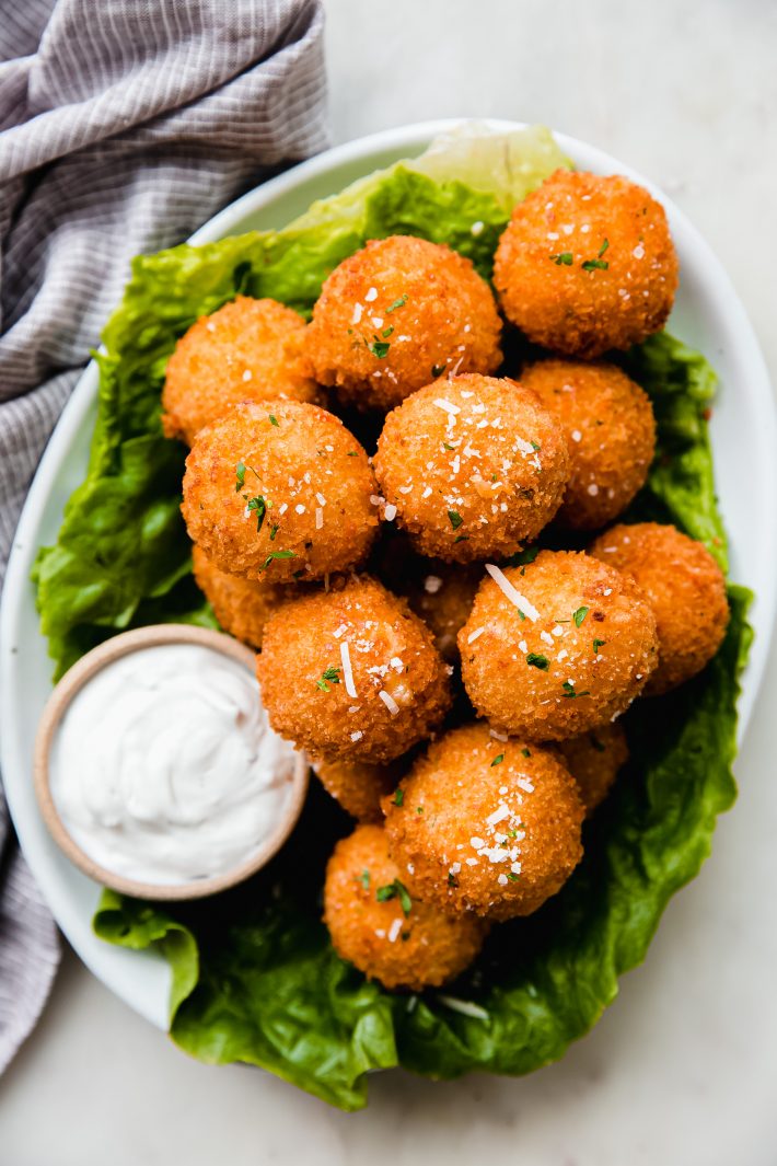 mashed potato balls on lettuce on white plate with dip