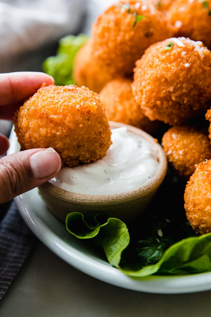 hand holding mashed potato ball and dipping in dip