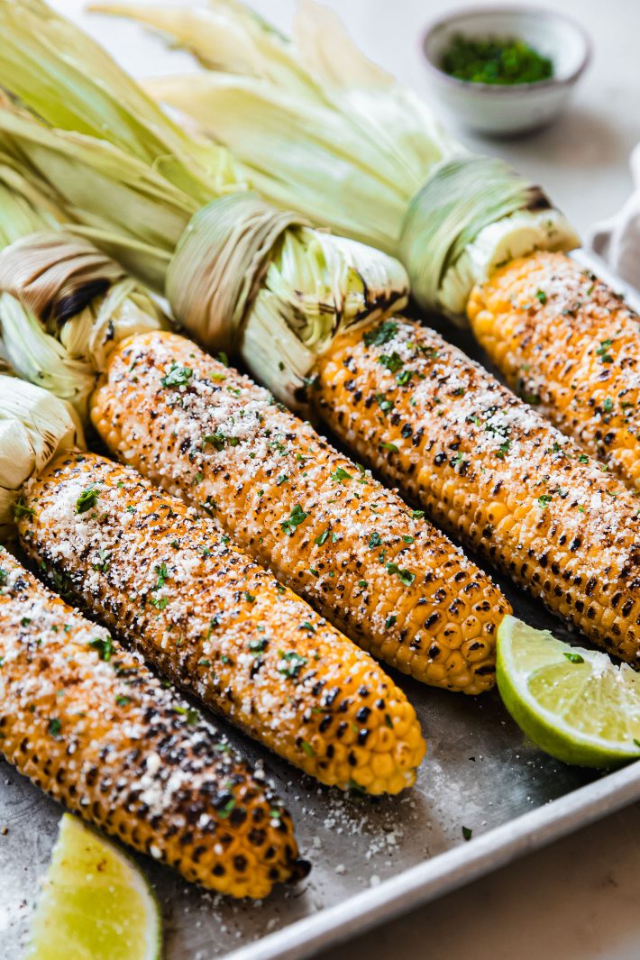 elotes on plate topped with cotija, cilantro, and chili powder