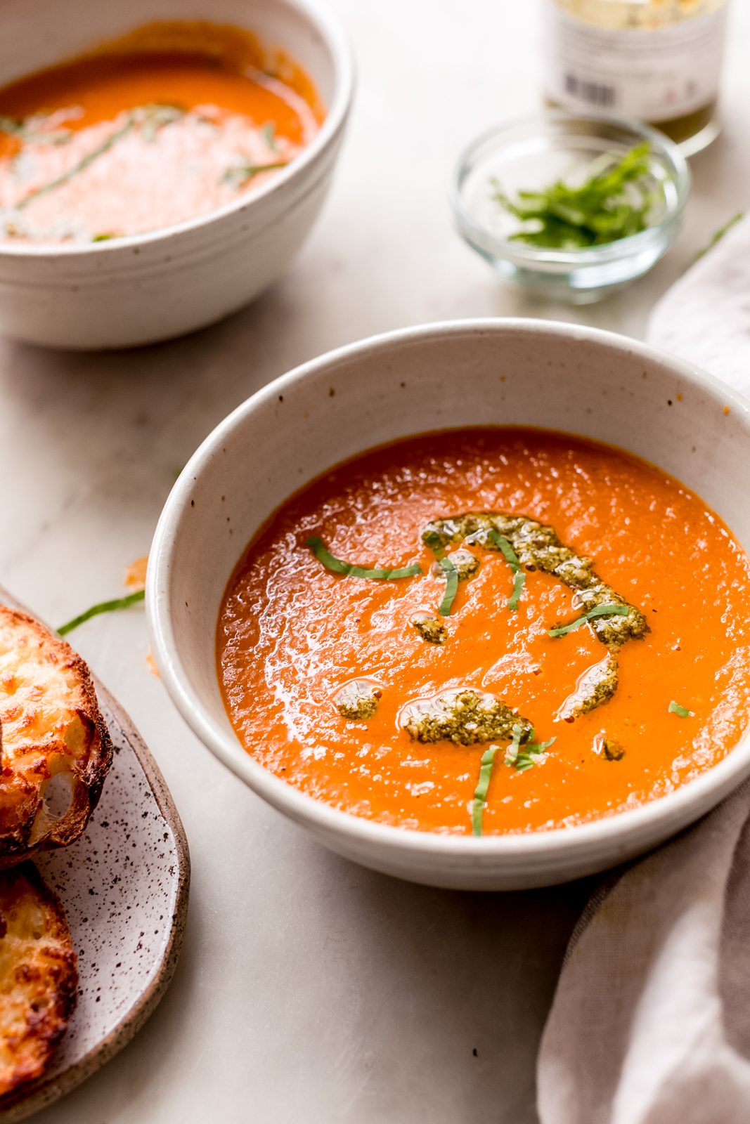 food scene with bowl of tomato basil soup with pesto and fresh basil on top