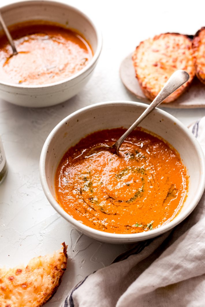 bowls of tomato basil soup with toasted cheesy bread on white surface