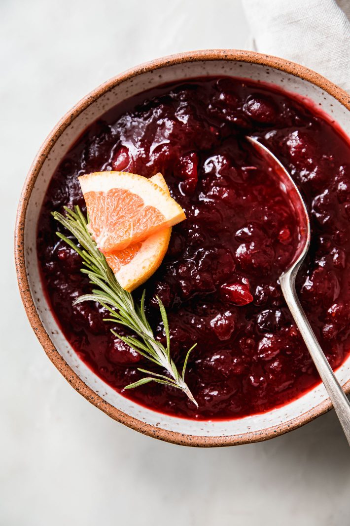 homemade cranberry sauce in bowl with orange slices and rosemary