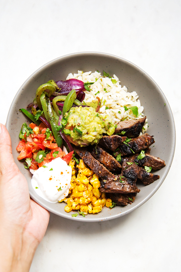 Homemade steak fajita bowls with garlic lime rice. These fajita bowls taste even better than the ones at Chipotle! The secret is the homemade marinade for the steak... it is to DIE for! #steakfajita #steakfajitabowls #fajitabowls #bowls | littlespicejar.com
