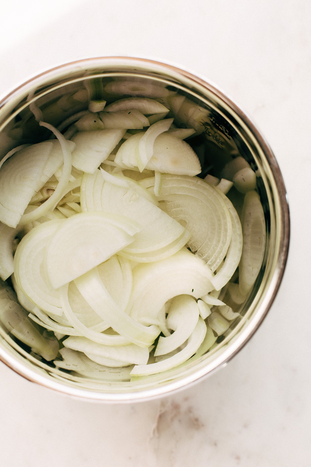 thinly sliced onions in stainless steel bowl