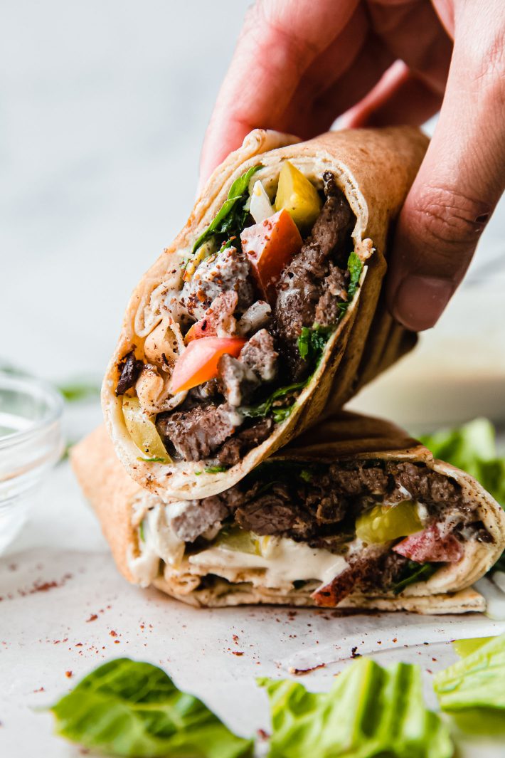 beef shawarma sandwich cut in half and stacked with hand