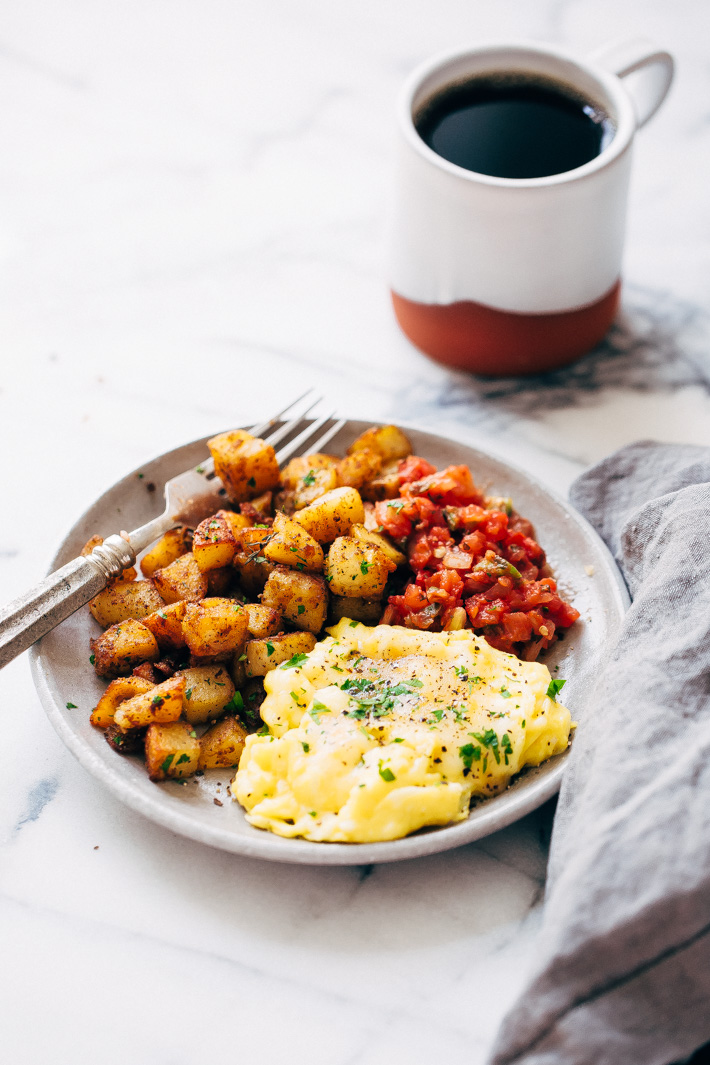 breakfast scene with pan fried potatoes, scrambled eggs, salsa and coffee on the side