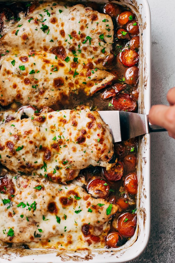 lifting melty cheese topped chicken breast from white baking dish