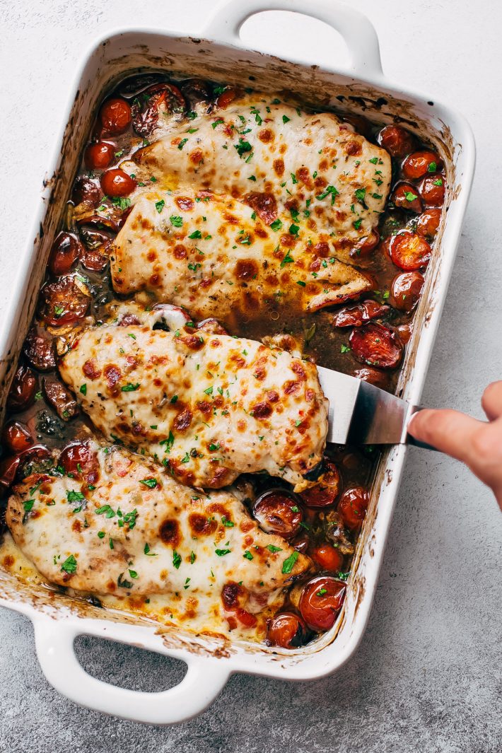 cheesy chicken breast being lifted with spatula from garlic butter tomato pan sauce