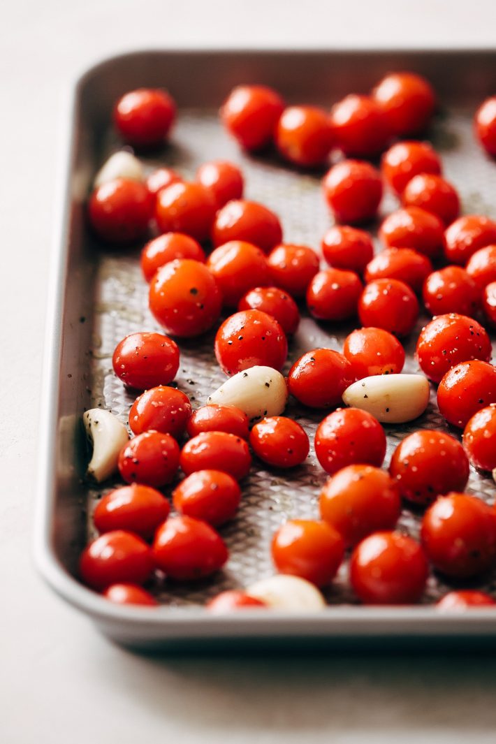 tomatoes on baking sheet with garlic cloves