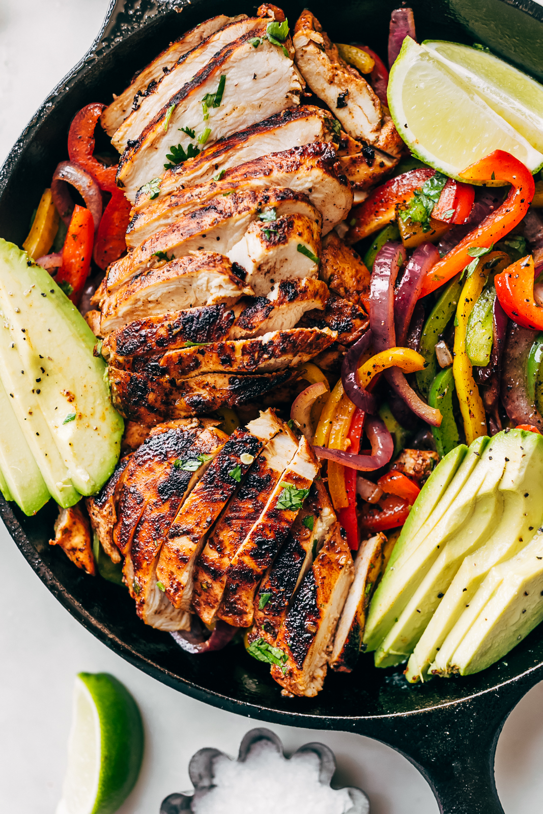 sliced chicken fajitas in a skillet with slice avocados and sautéed peppers and onions