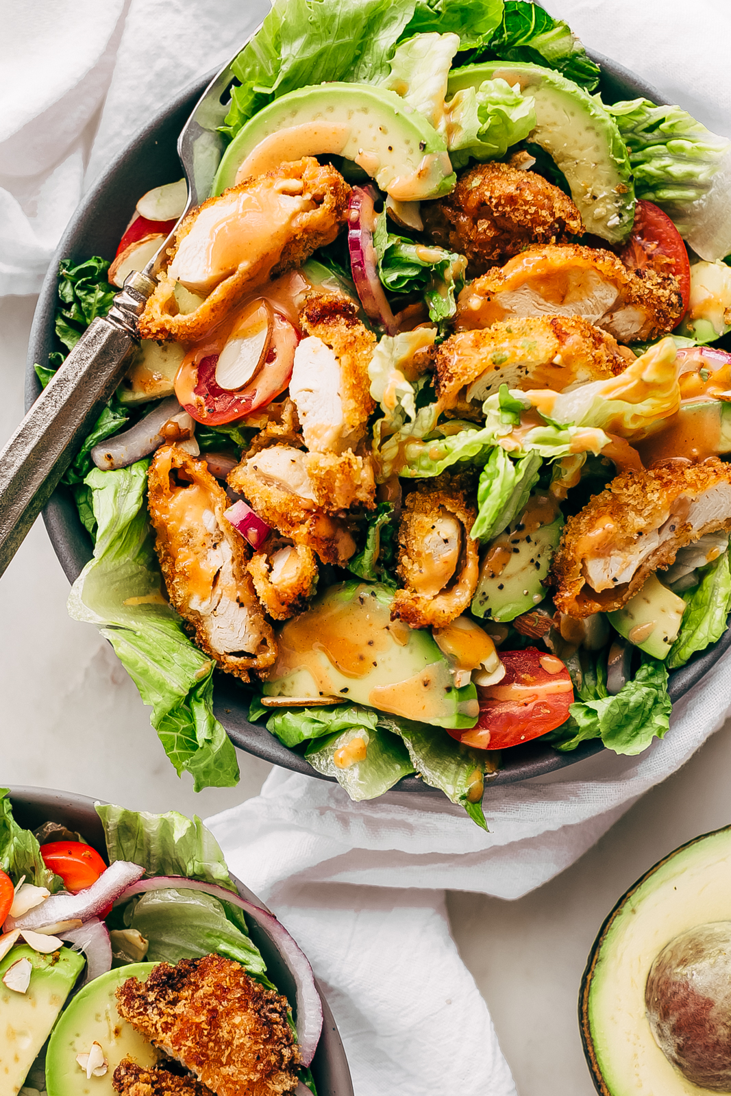 bowls of romaine topped with avocado slices, red onions, crispy chicken strips, almonds, and grape tomatoes