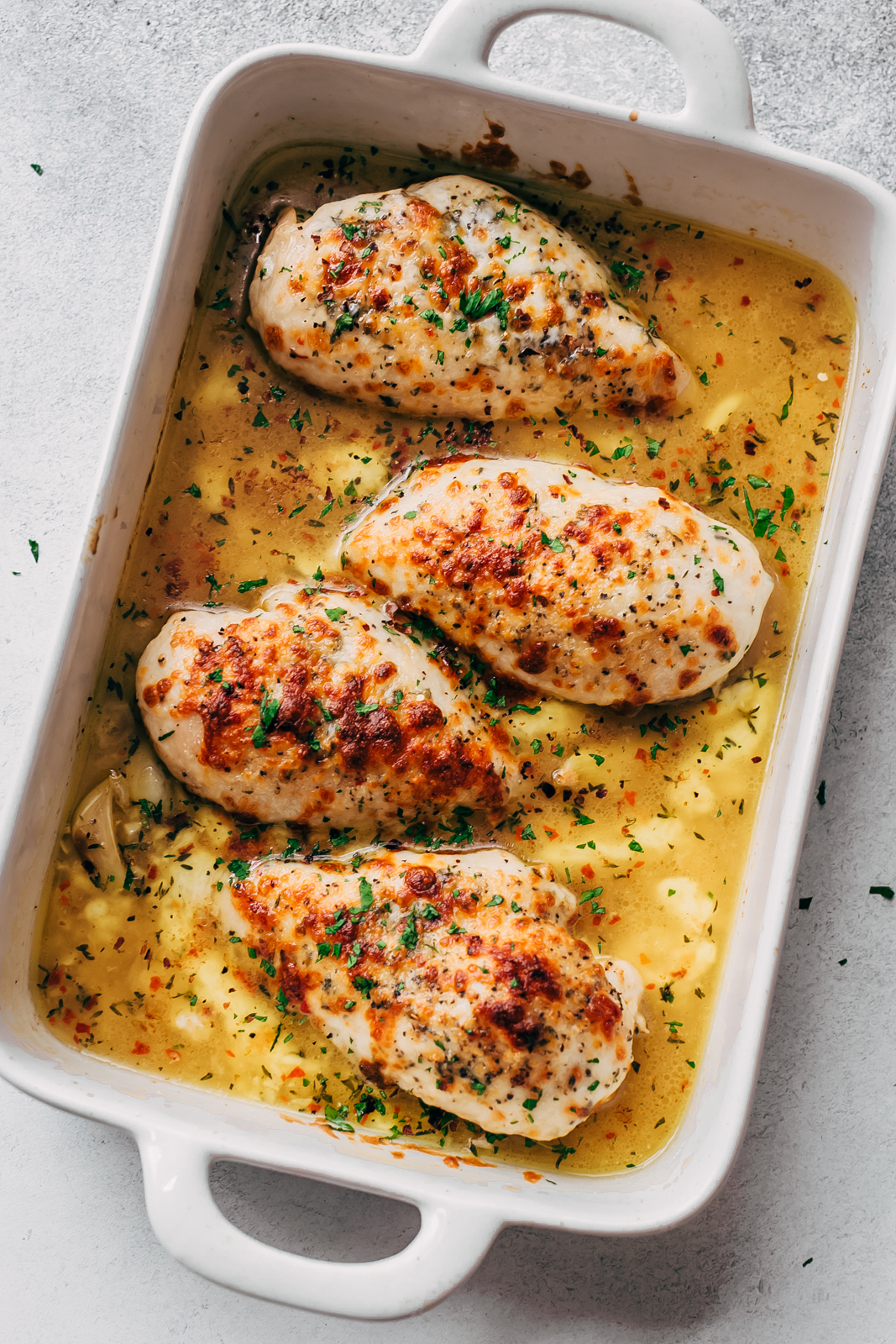 prepared garlic butter chicken topped with melted mozzarella in white baking dish