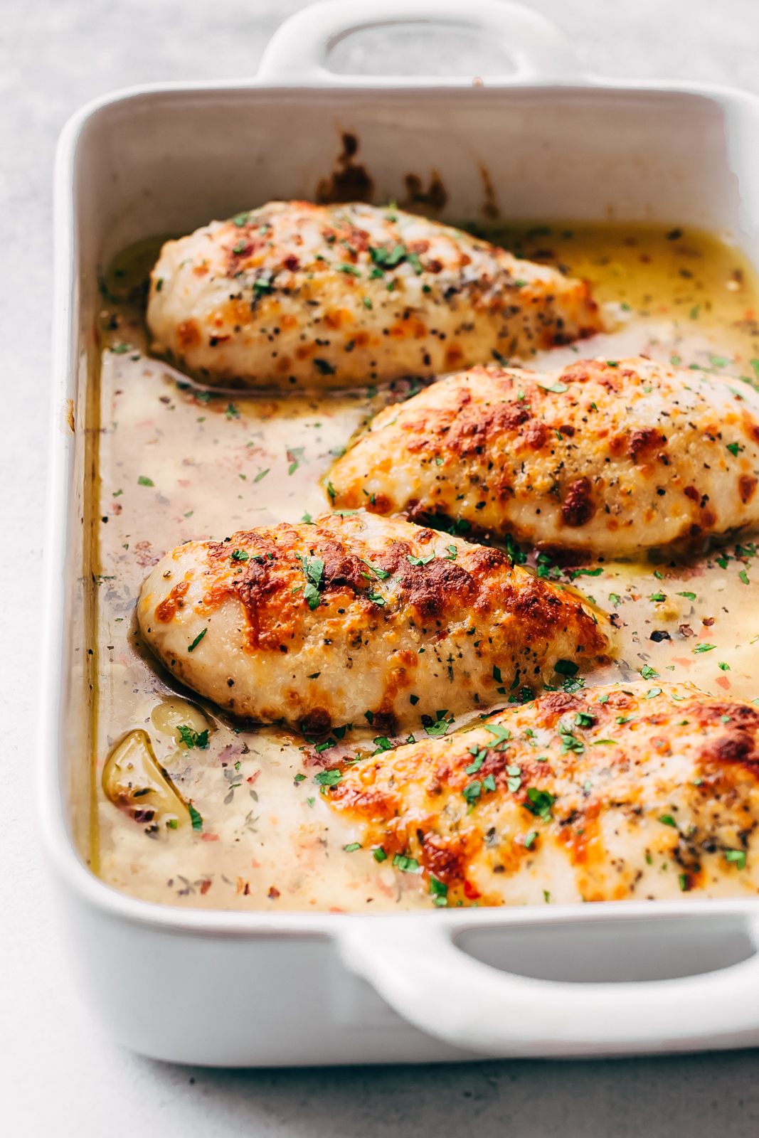 garlic butter sauce with roasted chicken breast with melted cheese in white baking dish