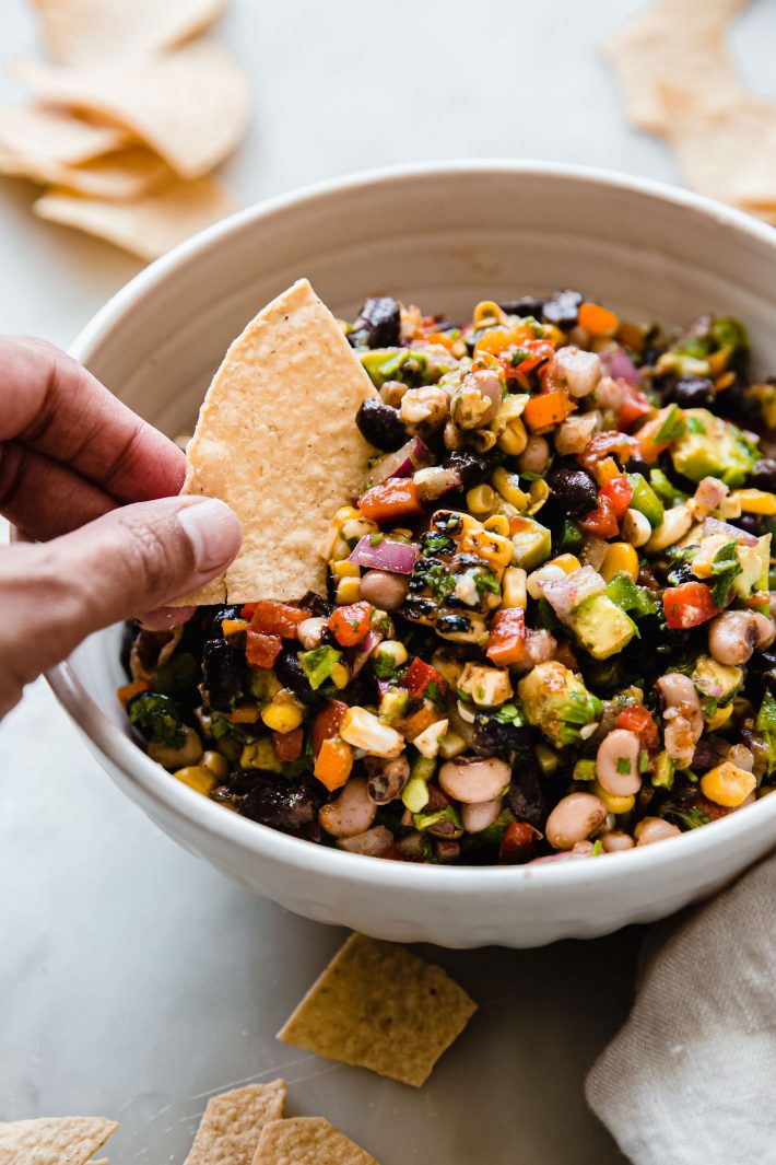 cowboy caviar in bowl with hand dipping tortilla chip