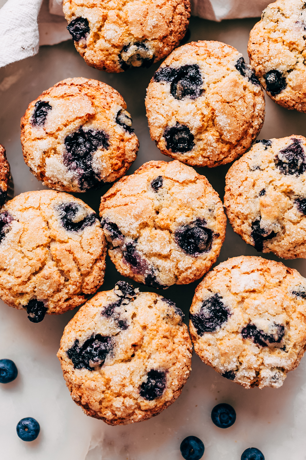 muffins gathered together on white marble with a few fresh blueberries scattered