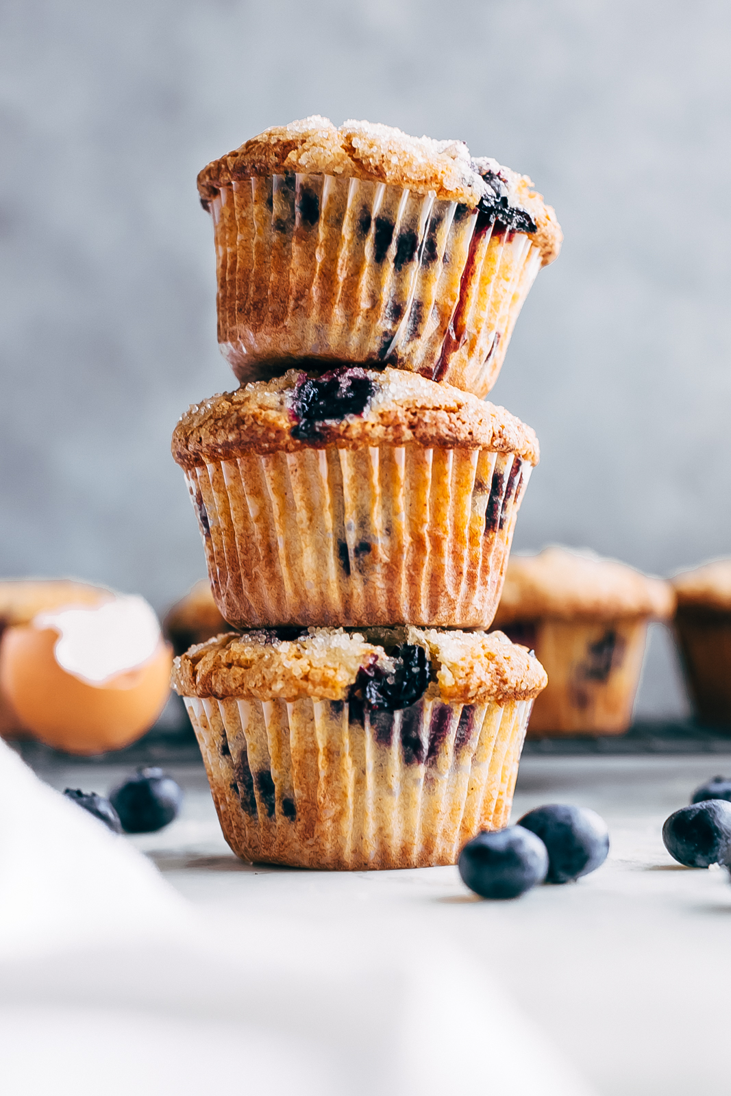 a tower of gluten-free blueberry muffins on white marble surrounded by muffins in the back