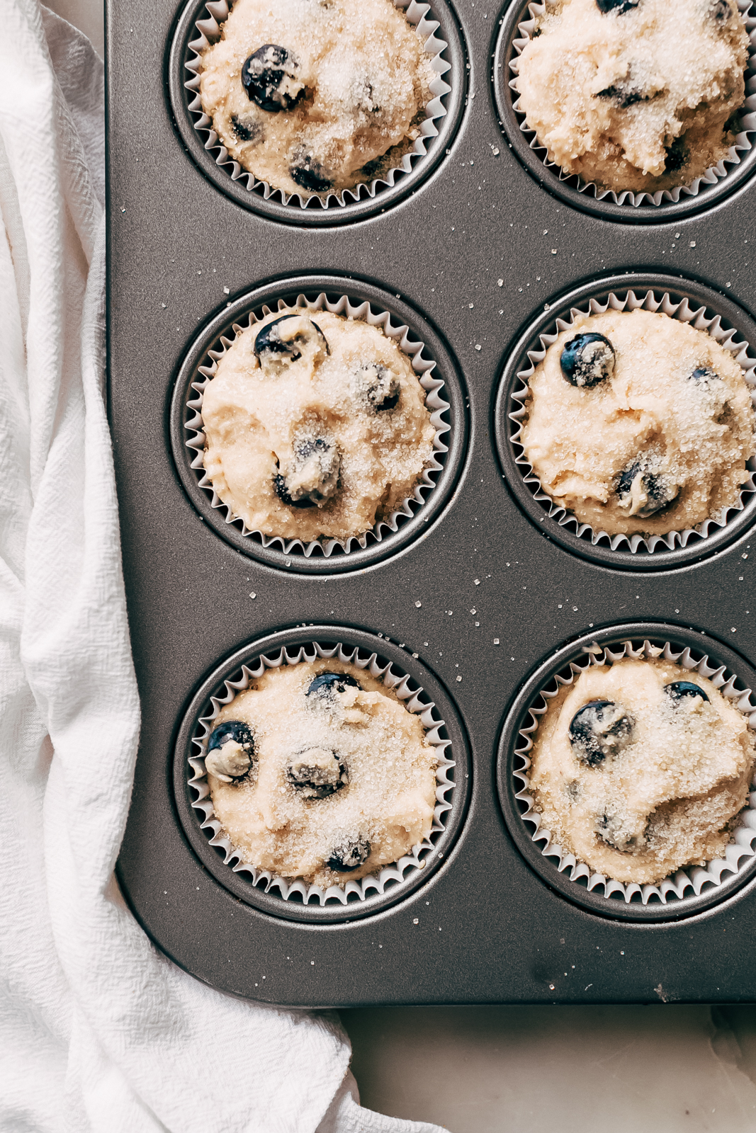 blueberry muffin batter topped with berries and sugar in muffin pan