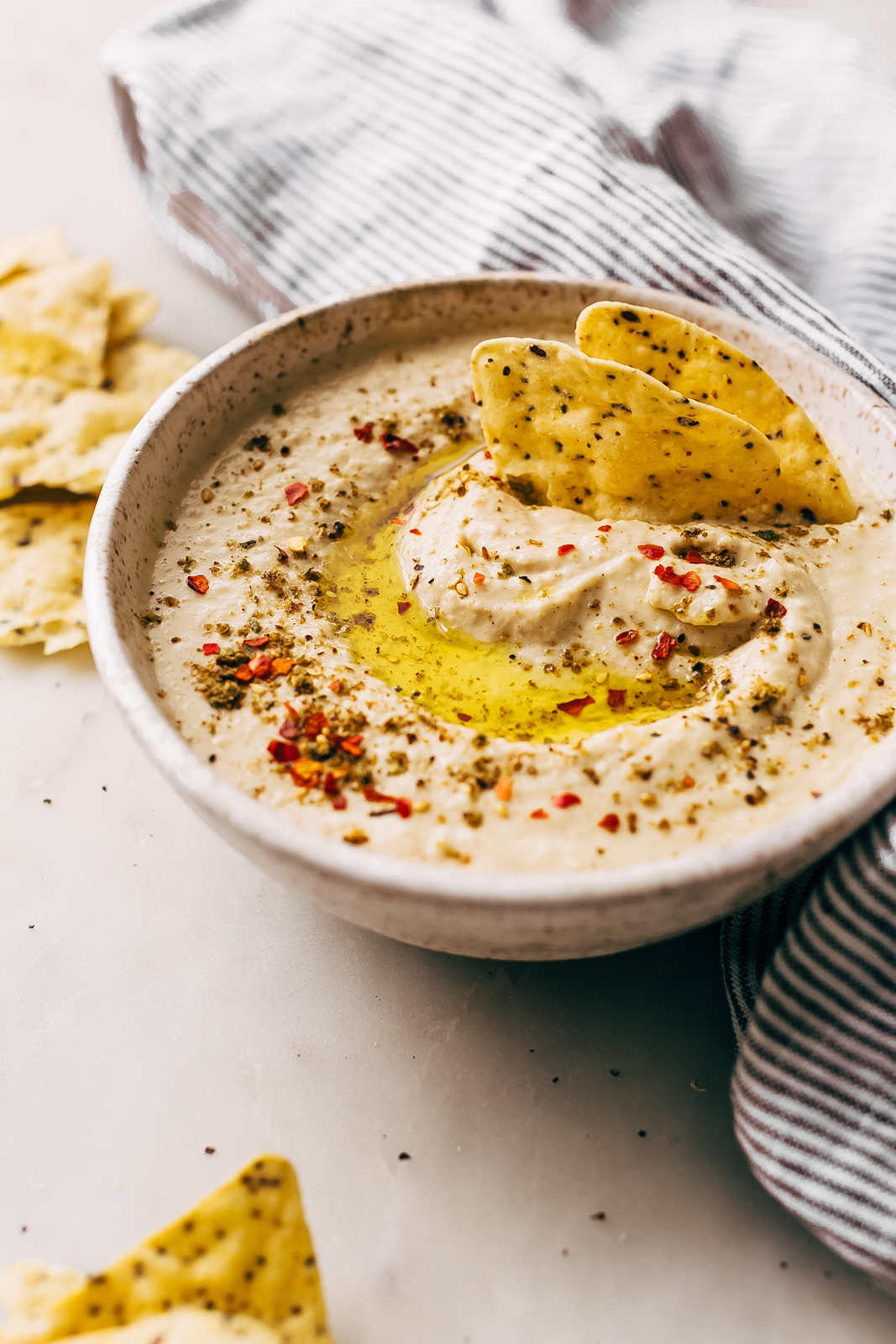 hummus in speckled bowl with zaatar and red pepper flakes on top with tortilla chips