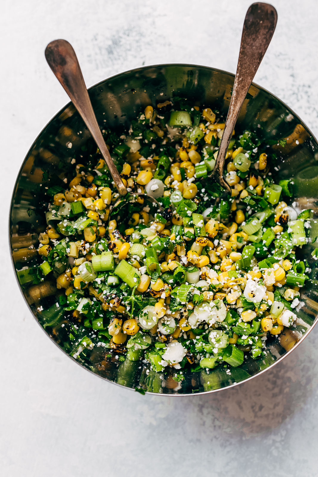 charred corn, scallions, cotija cheese in metal bowl with spoon and fork