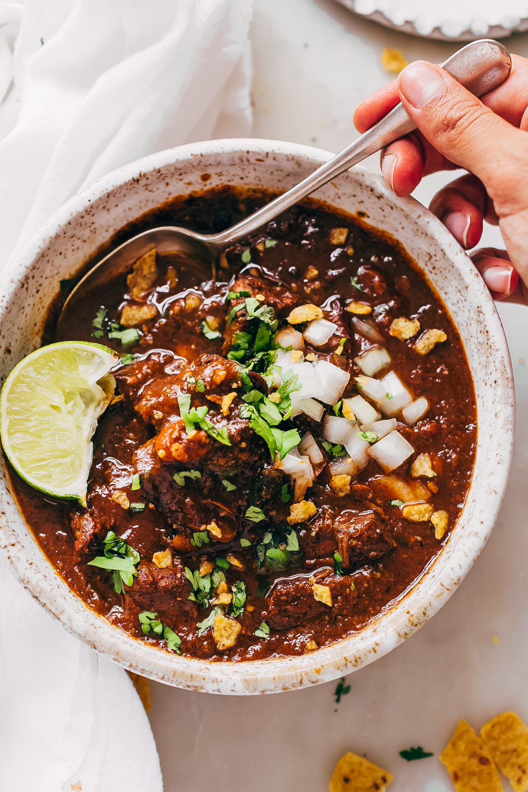 top shot of bowl filled with prepared stew meat chili with a hand holding a spoon in bowl