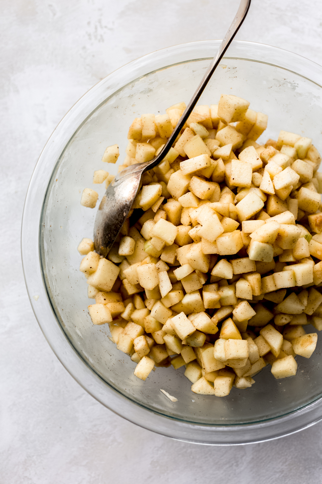 diced apples tossed with cinnamon in clear bowl with a spoon on grey surface