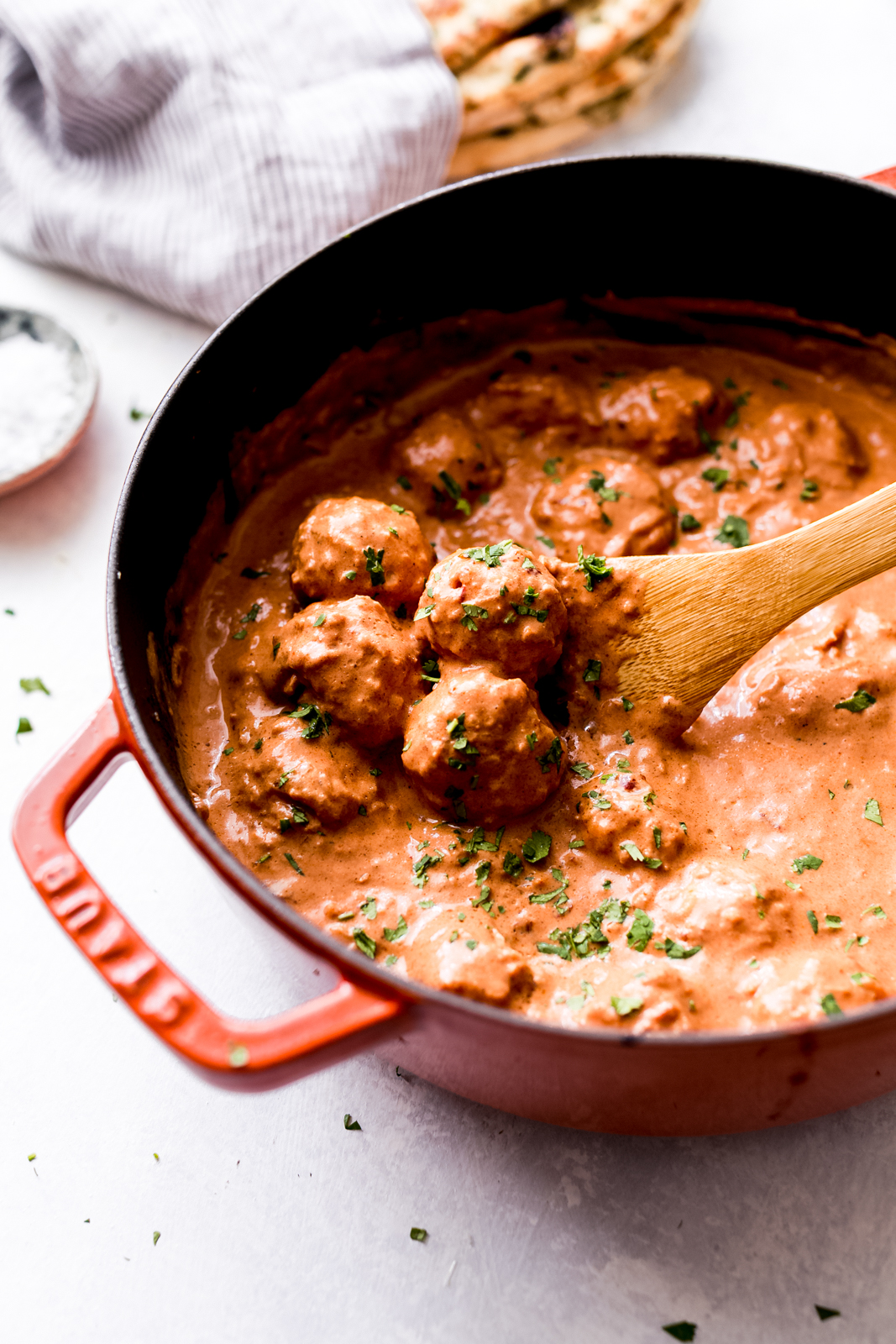 cast iron pot with chipotle butter chicken meatballs in sauce with wooden spoon 