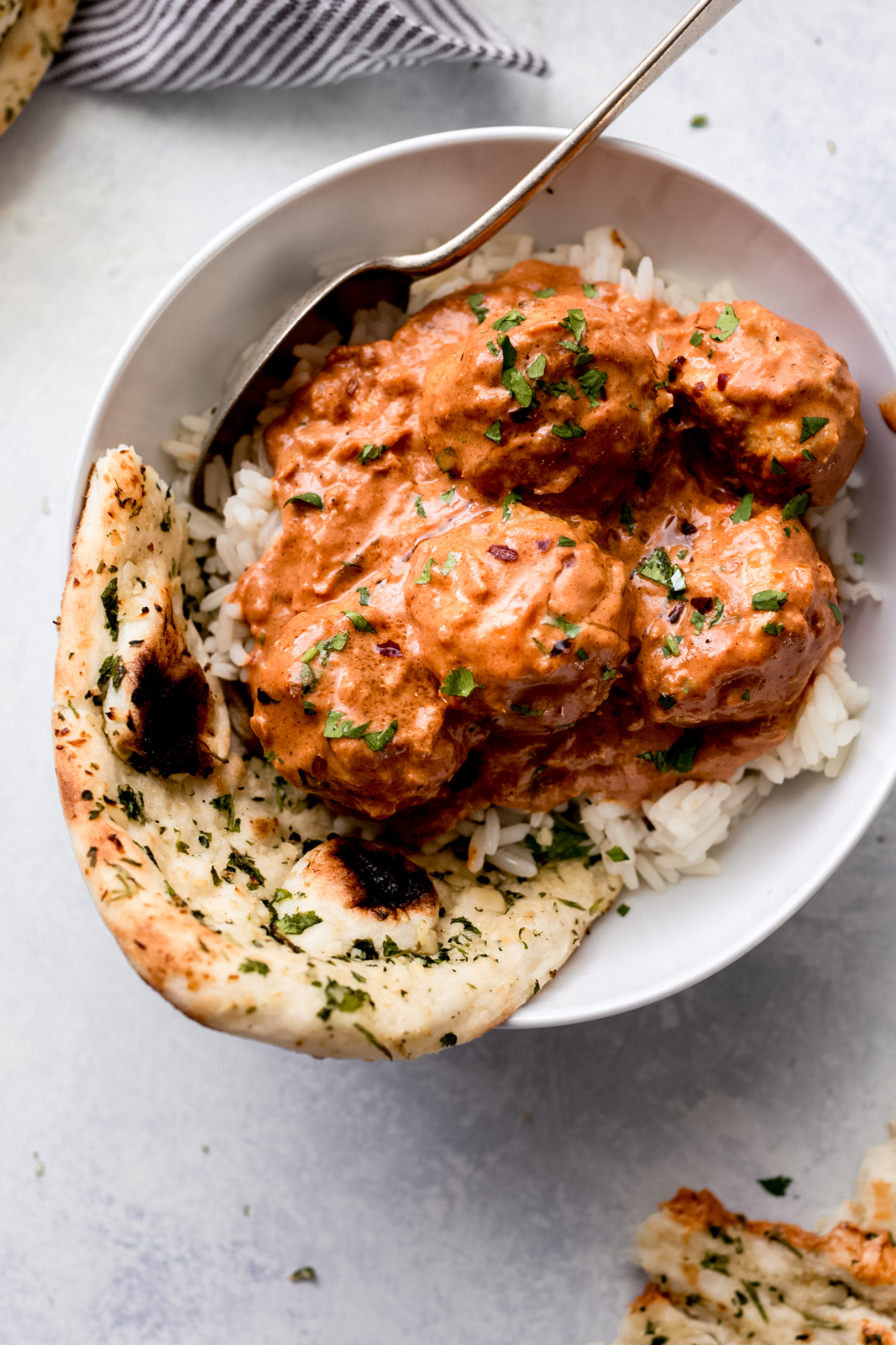 close up of meatballs in sauce over rice with torn garlic naan and spoon 