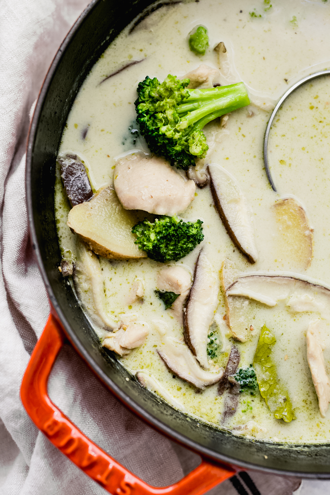 soup in cast iron pot showing slices of ginger, broccoli florets, chicken, and shiitake mushrooms