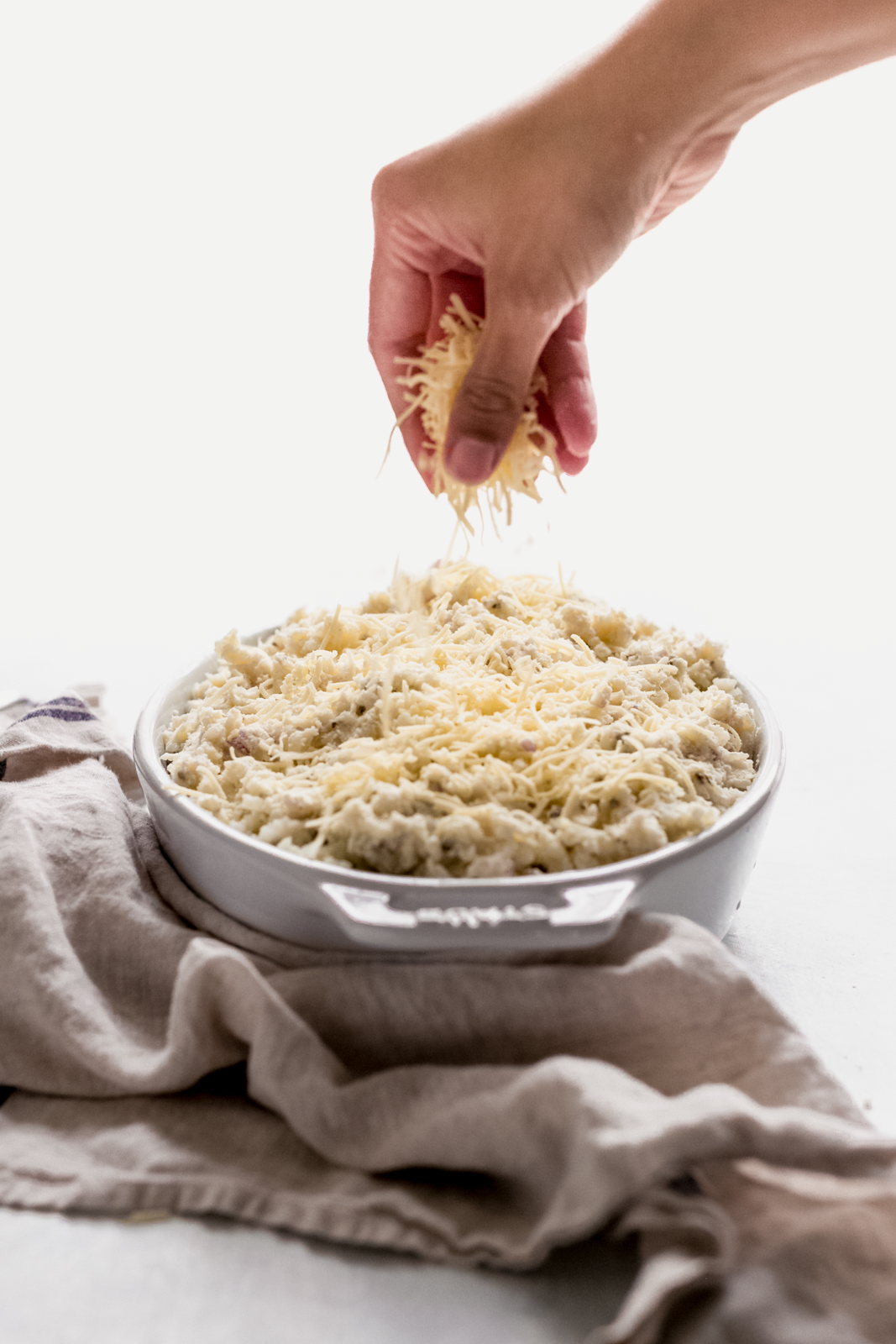 hand sprinkling cheese on fluffy potatoes in casserole dish