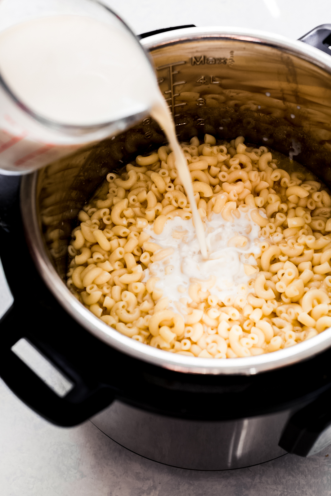pouring milk into instant pot with cooked elbow macaroni
