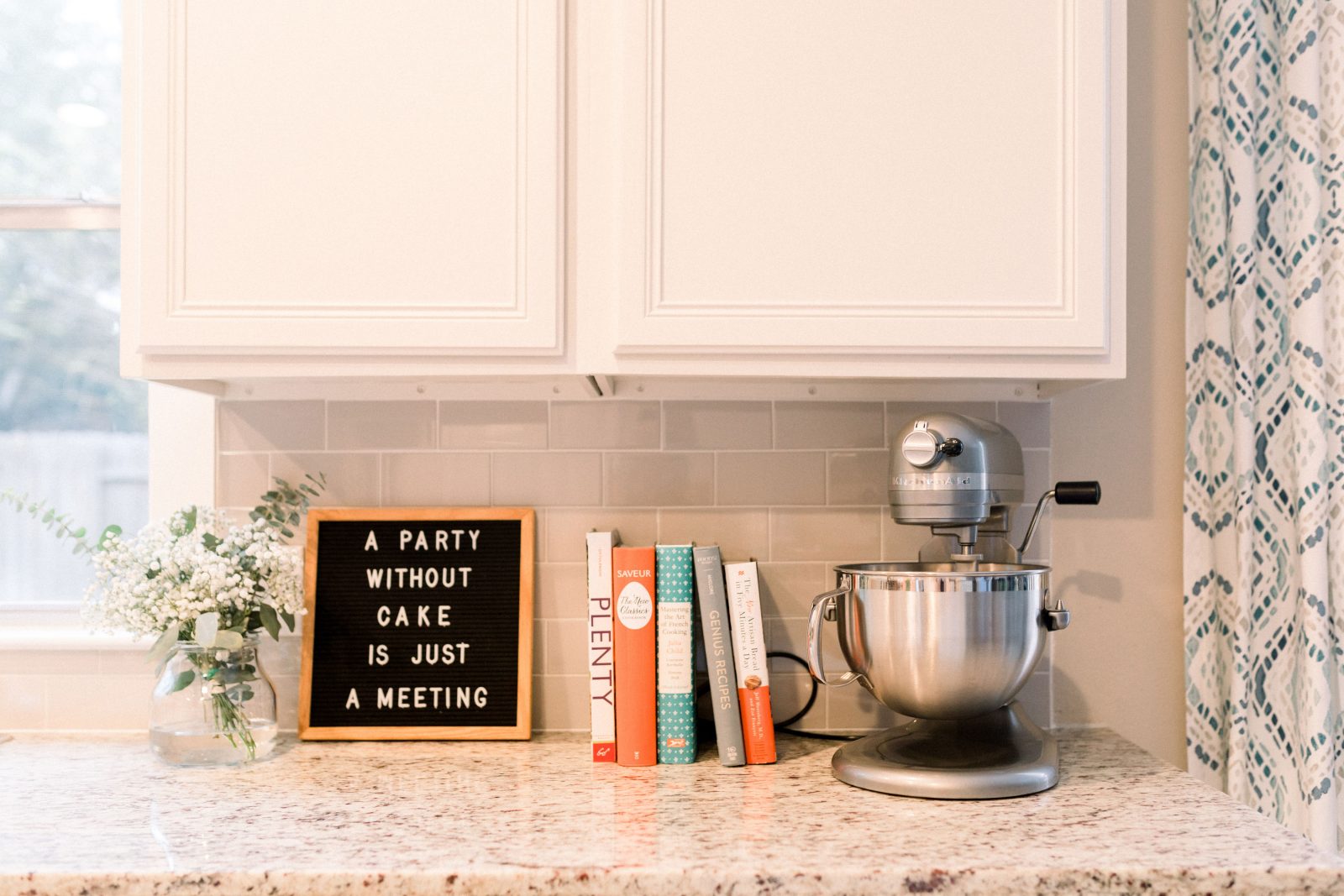 kitchen picture with books, stand mixer, and sign that read "a party without cake is just a meeting'