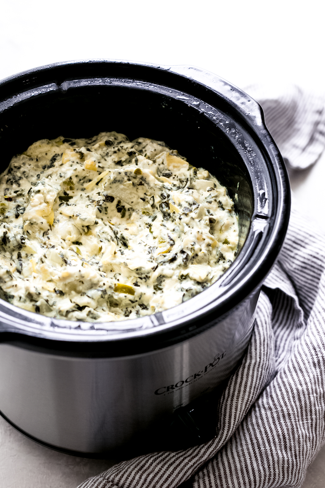 slow cooker spinach artichoke dip prepared in slow cooker with striped towel