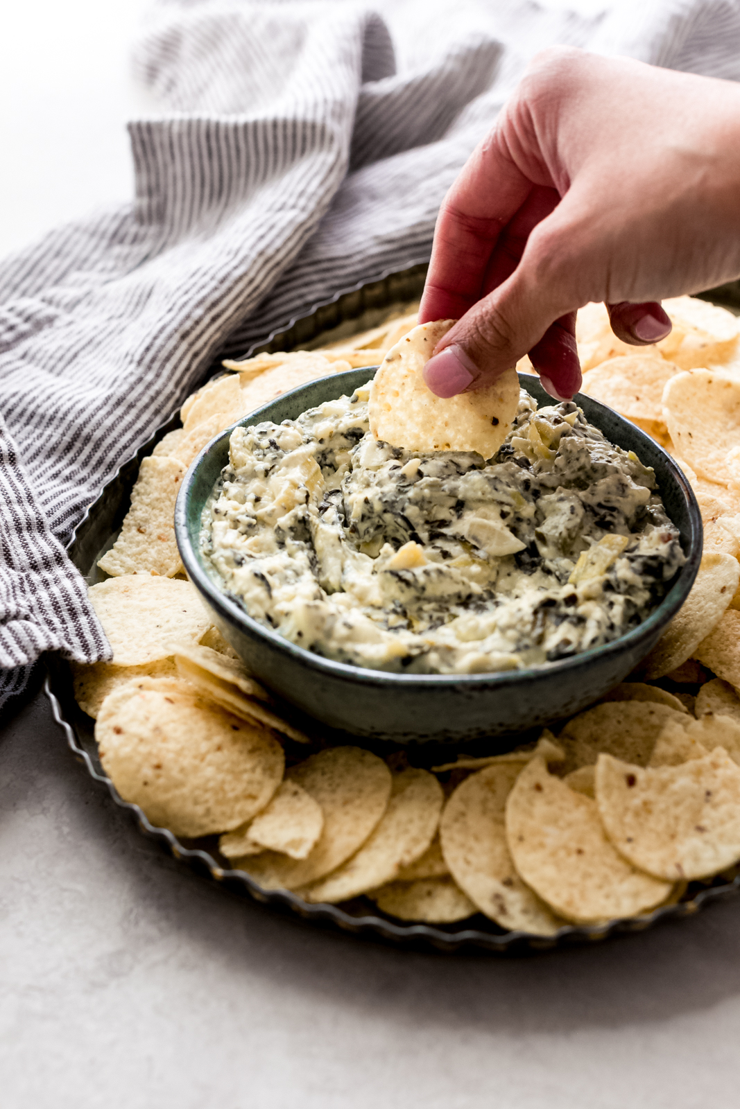 hand dipping chip on prepared dip in bowl on serving tray with tortilla chips surrounding it