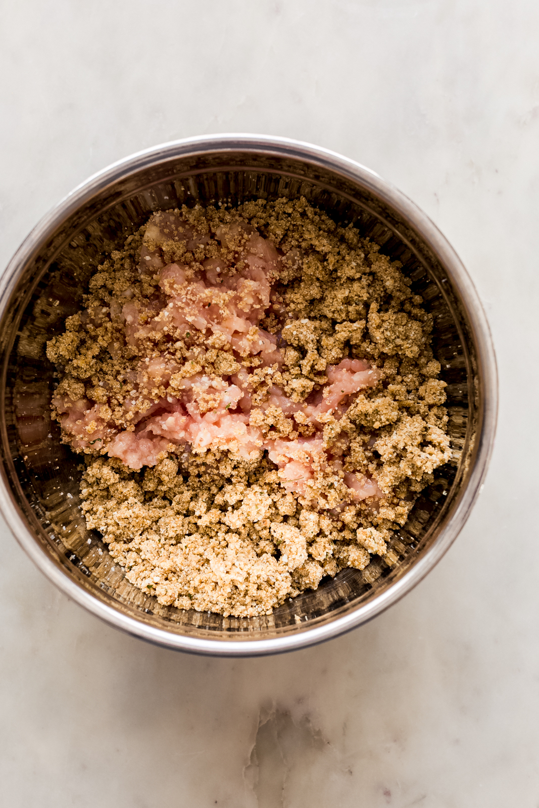 mixing the ground chicken with breadcrumbs to make meatballs in metal bowl