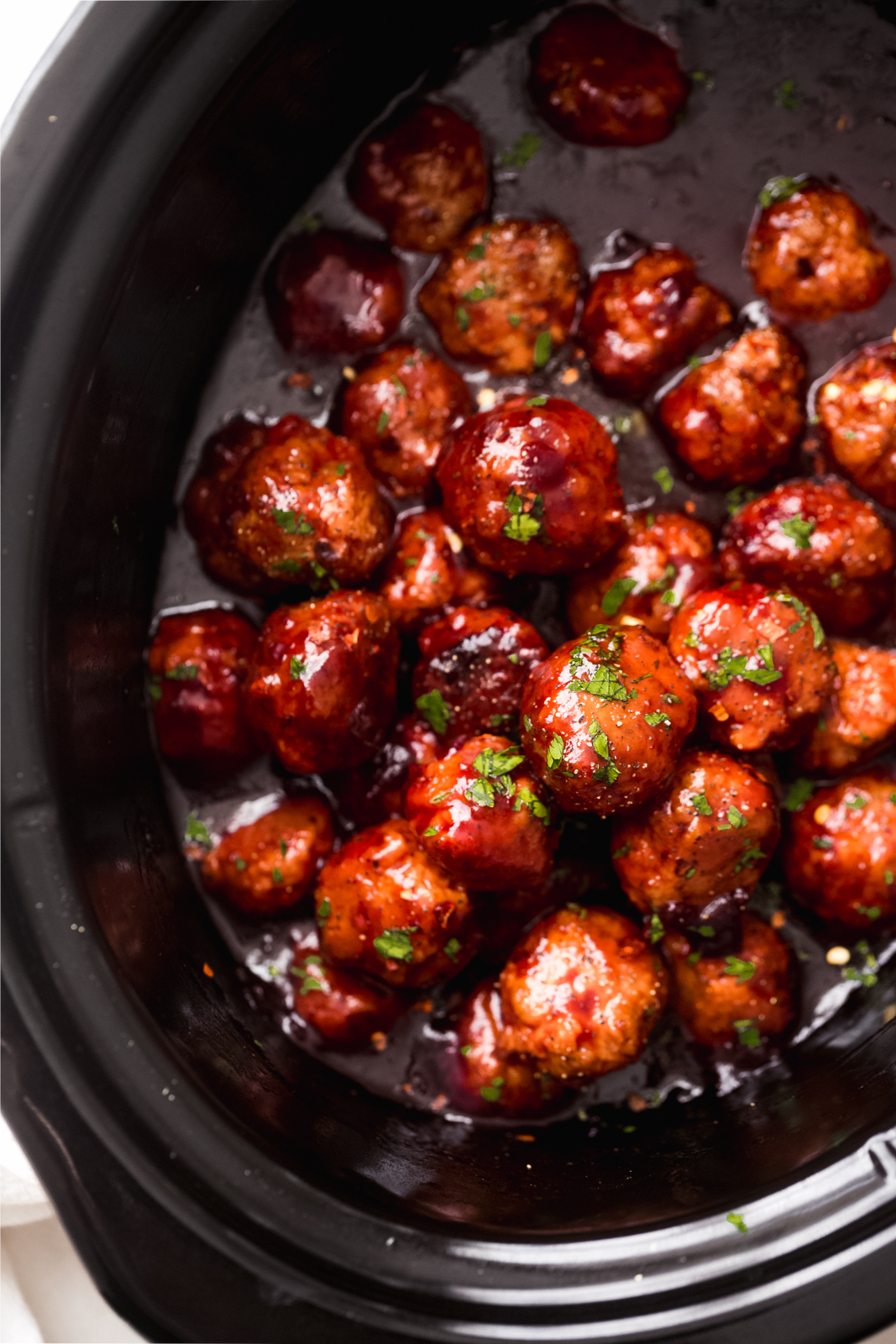 slow cooker with sauce and chicken meatballs topped with parsley