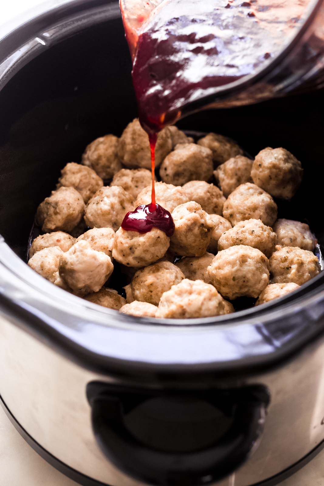 slow cooker loaded with cooked meatballs being drizzled with bbq honey chipotle sauce