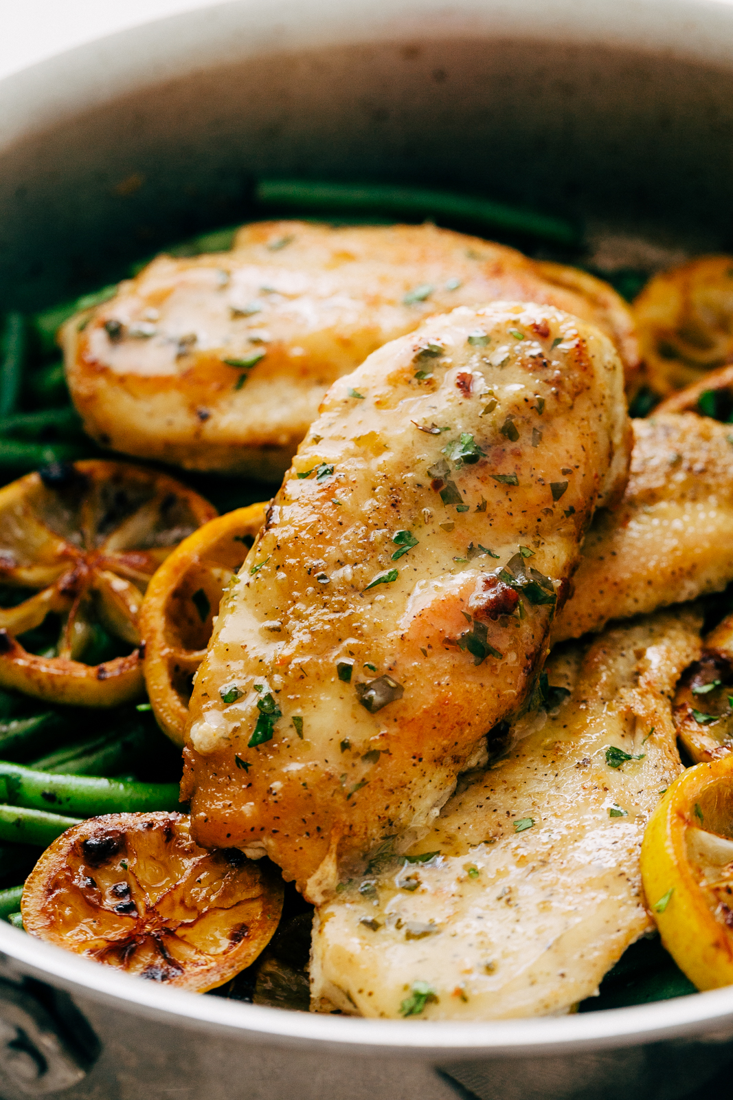 close up of lemon butter drizzled chicken breast in pan