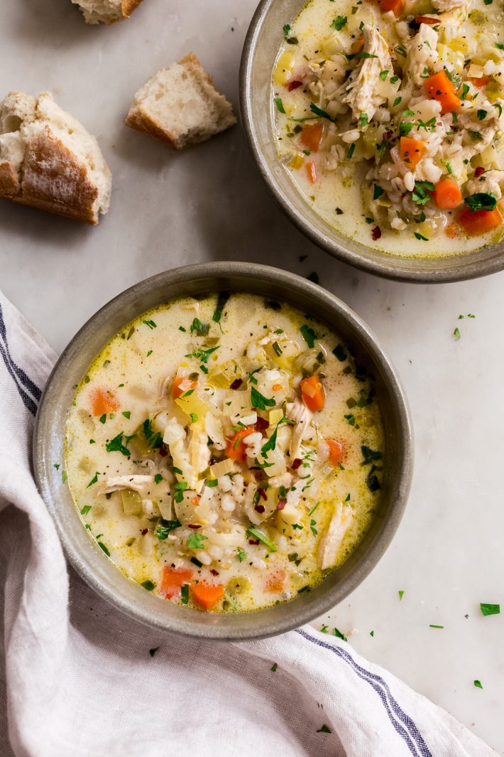 bowls of chicken barley soup on white marble surface