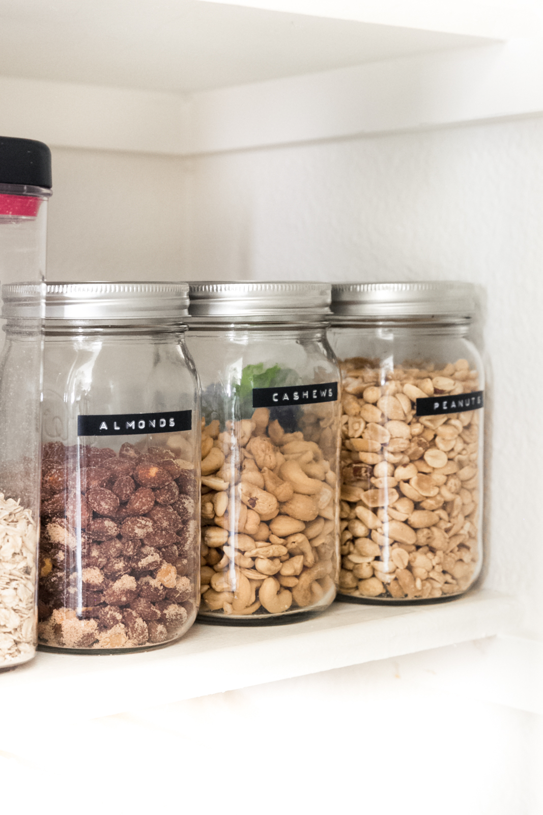 three mason jars holding nuts that are labeled with black labels with white letters
