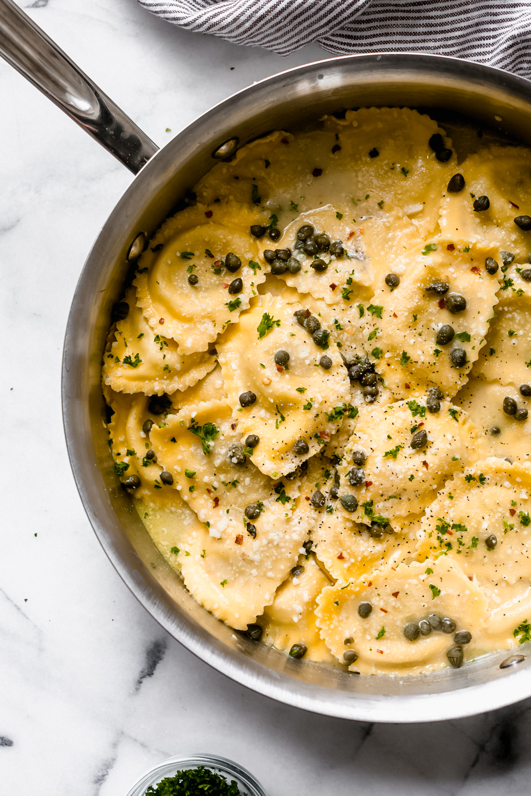 skillet with ravioli in piccata sauce sprinkled with capers
