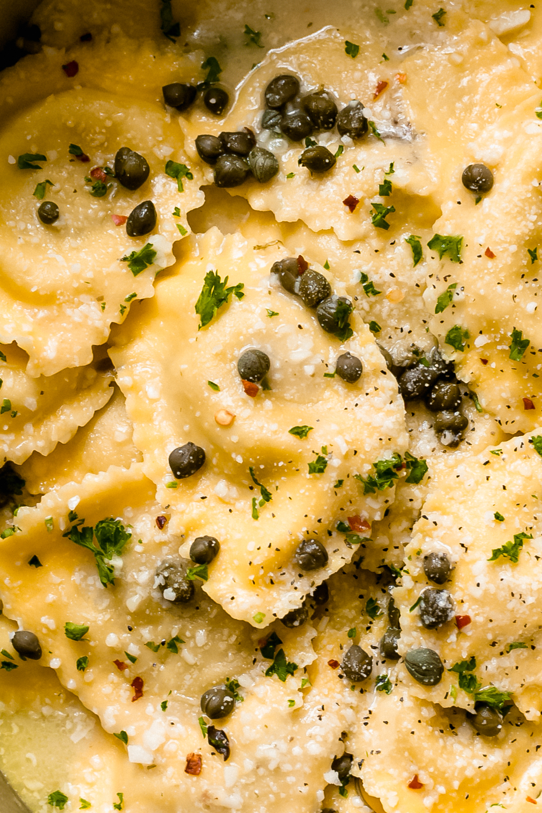 close up shot showing texture of ravioli in lemon butter sauce sprinkled with capers and parmesan cheese