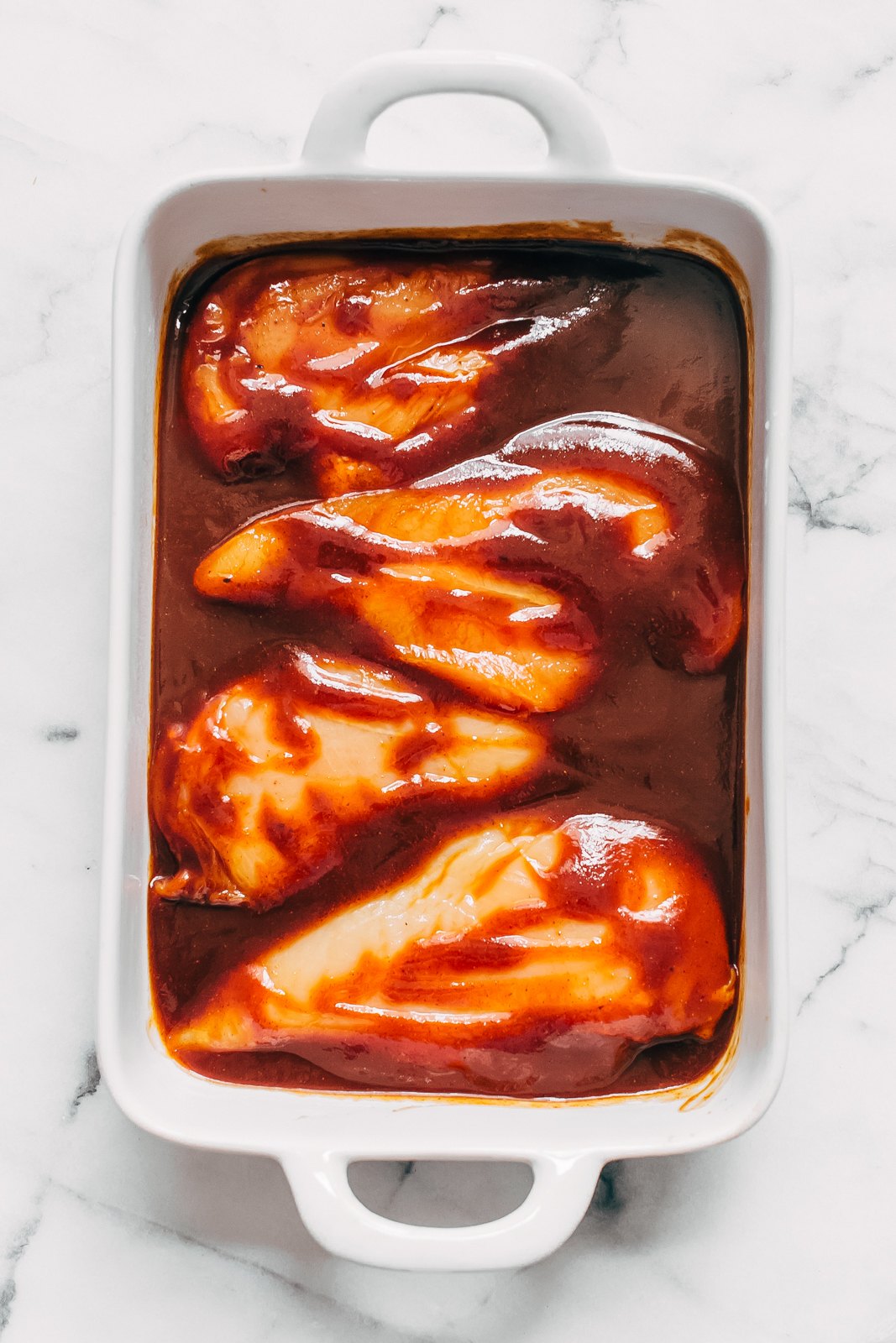 white dish with bbq sauce dipped raw chicken before cooking