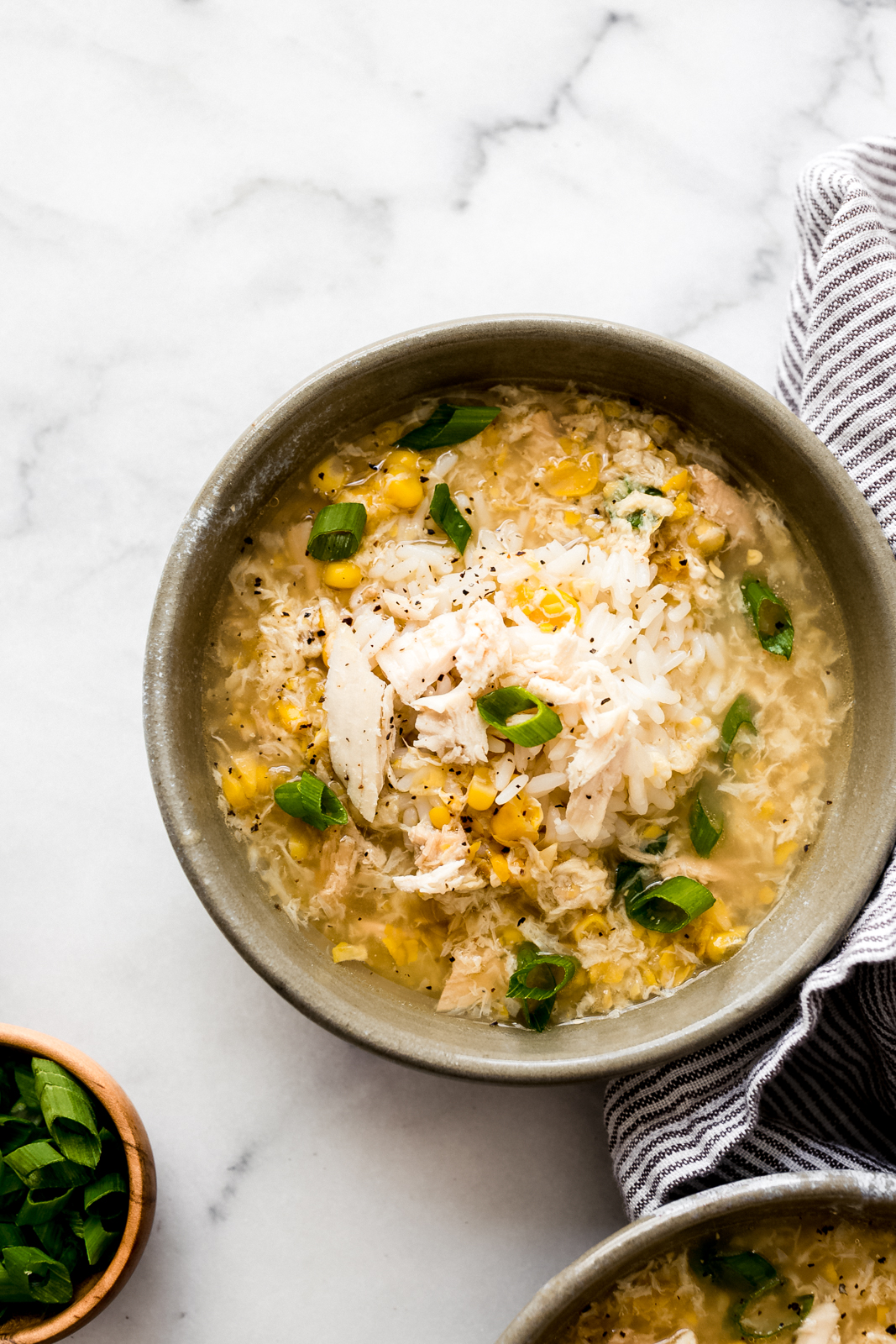 bowl of chicken corn soup topped with shredded chicken and a scoop of rice with scallions sprinkled on top
