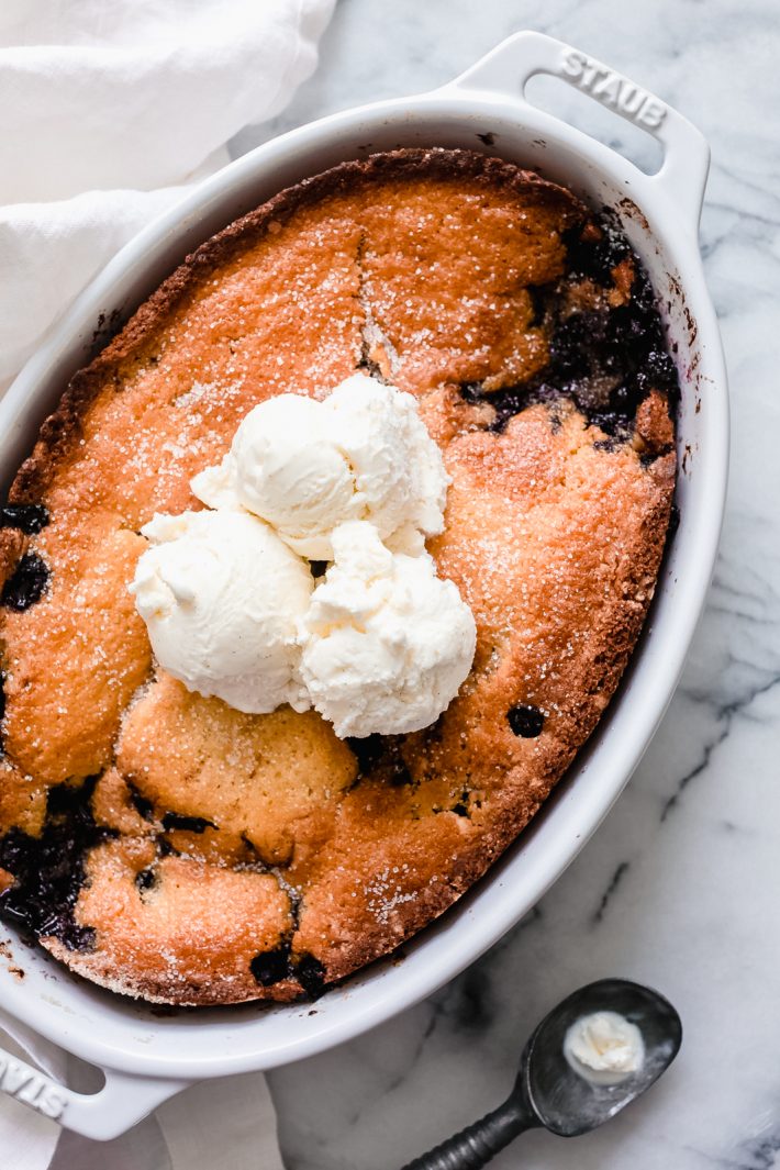 oval baking dish with blueberry cobbler topped with three scoops of vanilla ice cream