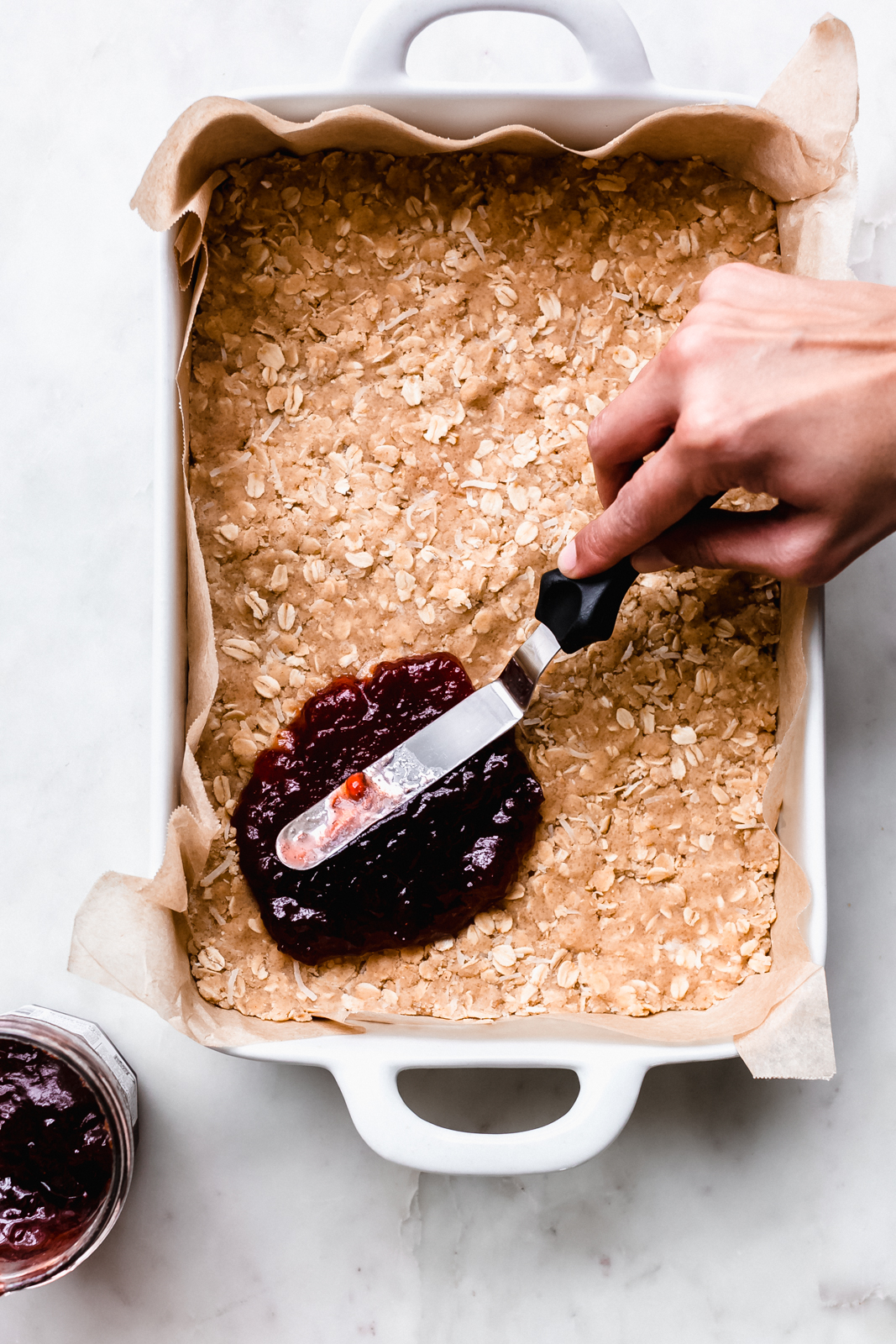 spreading jam with offset spatula on the bottom oat crust